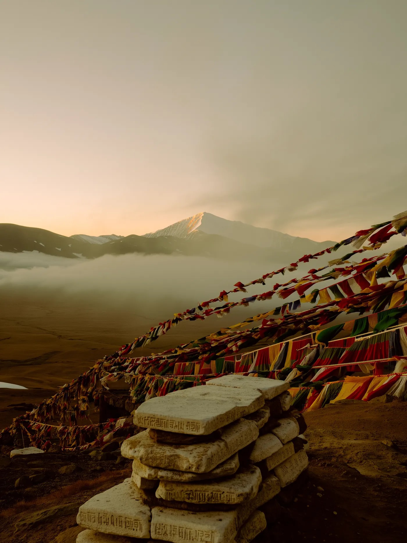 Mani stones carved with mantras and strings of prayer flags on a misty mountain pass